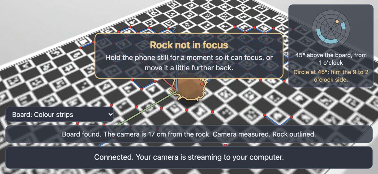 The phone's screen with the board sharp in the distance, the rock blurred, and a box above it reading Rock not in focus, Hold the phone still for a moment so it can focus, or move it a little further back.